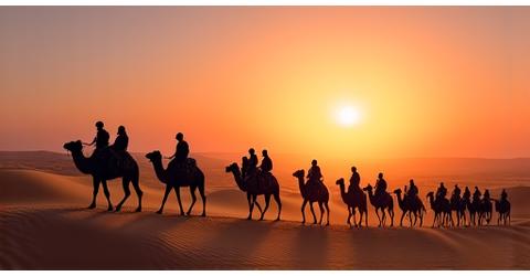 A line of camels with riders gracefully moving across desert dunes during sunset